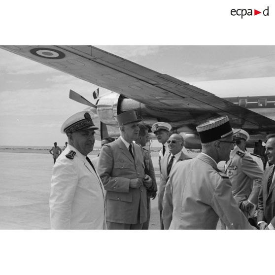 Le général Charles De Gaulle, président de la République, et le le vice-amiral Jean Lorain, commandant du groupe opérationnel des expérimentations nucléaires (GOEN), au pied de l'avion à l'aéroport de Moruroa. En arrière-plan, Pierre Billotte, ministre des Départements et territoires d'Outre-mer, et Alain Peyrefitte, ministre de la Recherche scientifique et des Questions atomiques et spatiales.