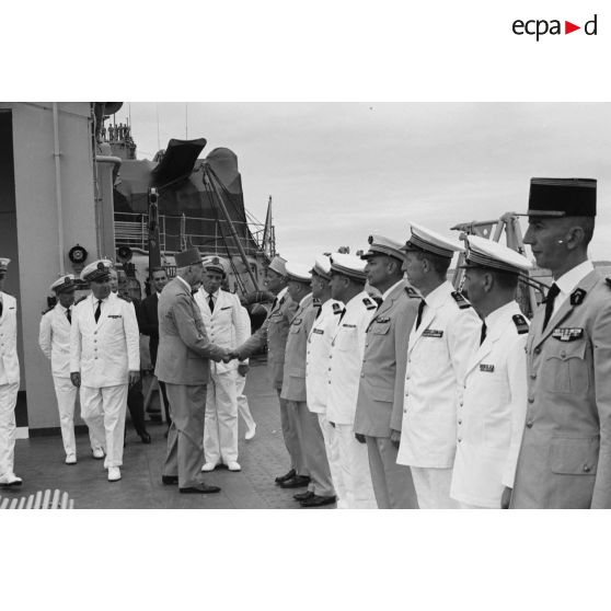 Le général Charles De Gaulle, président de la République, salue des officiers supérieurs aux côtés du capitaine de vaisseau Michel Teisserenc, commandant du croiseur De Grasse, et du vice-amiral Jean Lorain, commandant du groupe opérationnel des expérimentations nucléaires (GOEN).