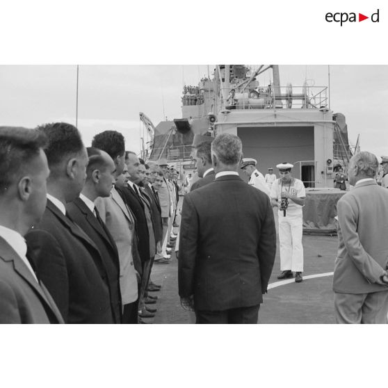 Le général Charles De Gaulle, président de la République, salue des personnels civils à bord du croiseur De Grasse, suivi par Pierre Messmer, ministre des Armées, et Alain Peyrefitte, ministre de la Recherche scientifique et des Questions atomiques et spatiales.