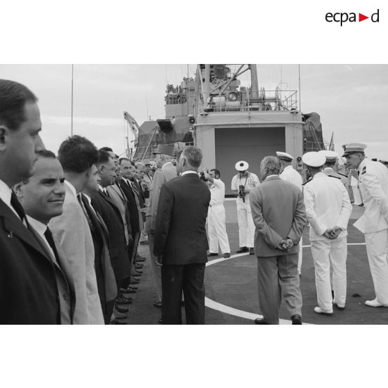 Le général Charles De Gaulle, président de la République, salue des personnels civils à bord du croiseur De Grasse, suivi par Pierre Messmer, ministre des Armées, et Alain Peyrefitte, ministre de la Recherche scientifique et des Questions atomiques et spatiales.