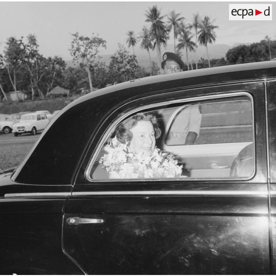 Mme Thabaud, épouse du nouveau directeur du Centre d'expérimentations du Pacifique (CEP),  colliers de fleurs autour du cou, dans une voiture à son arrivée à l'aéroport de Faa'a, 1964.