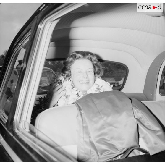 Mme Thabaud, épouse du nouveau directeur du Centre d'expérimentations du Pacifique (CEP),  colliers de fleurs autour du cou, dans une voiture à son arrivée à l'aéroport de Faa'a, 1964.