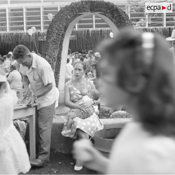 Fêtes du Juillet ou fête du Tiurai à Papeete en 1964. Portrait d'une jeune femme polynésienne allaitant un petit enfant.