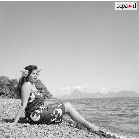 Fêtes du Juillet ou fête du Tiurai à Papeete en 1964. Portrait d'une jeune femme polynésienne au bord du rivage. En arrière-plan, l'île de Moorea.