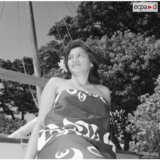 Fêtes du Juillet ou fête du Tiurai à Papeete en 1964. Portrait d'une jeune femme polynésienne devant une pirogue.