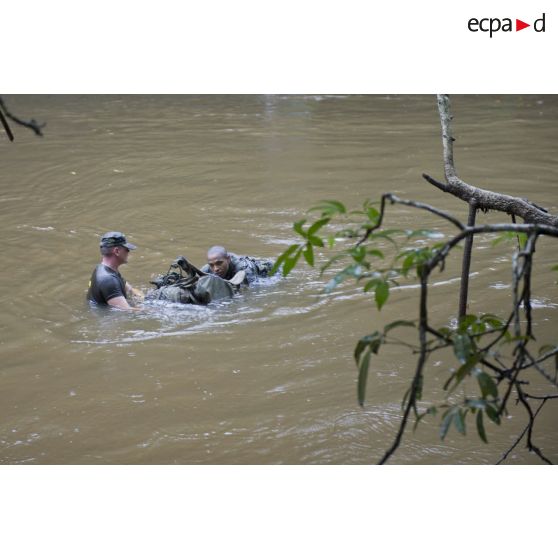 Un instructeur du 9e régiment d'infanterie de marine (9e RIMa) encadre un stagiaire pour la traversée d'une crique avec sac et armement sur la zone d'instruction de Tuff, en Guyane française.