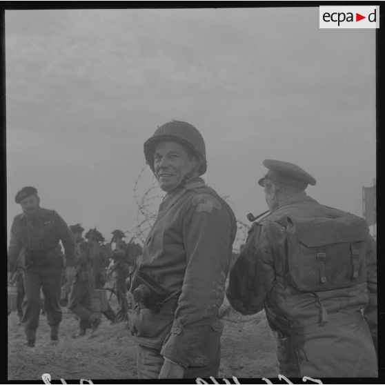 Sur le tournage du film Le jour le plus long. Portrait d'un acteur jouant le rôle d'un correspondant de guerre américain. De dos, acteur jouant le rôle d'un correspondant de guerre britannique (british war correspondant), tel Cornelius Ryan, auteur du livre The longest day.