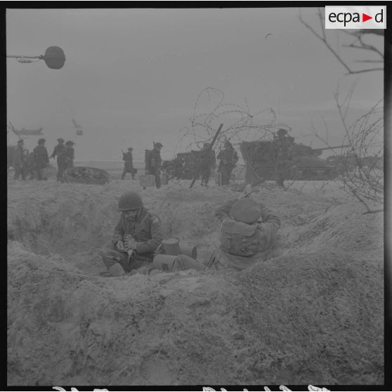 Sur le tournage du film Le jour le plus long. Acteur jouant le rôle d'un correspondant de guerre américain. De dos, acteur jouant le rôle d'un correspondant de guerre britannique (british war correspondant), tel Cornelius Ryan, auteur du livre The longest day.