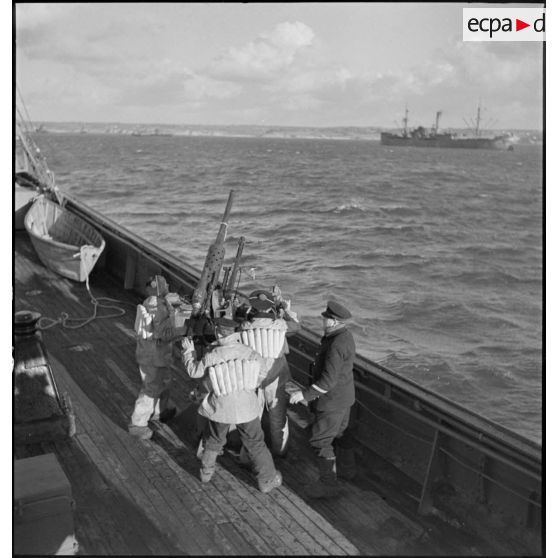 Des canonniers pointent un canon antiaérien de 37 mm à bord d'un cargo naviguant en convoi, réquisitionné et armé par la Marine nationale.