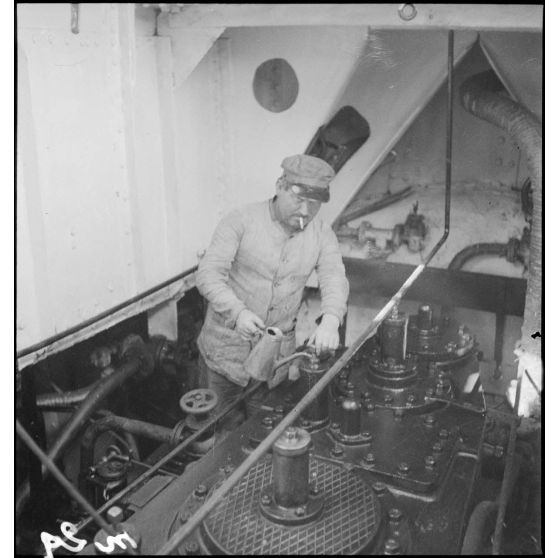 Un marin mécanicien huile des pièces dans la salle des machines du chalutier de la marine marchande Roche noire, réquisitionné par la Marine nationale.