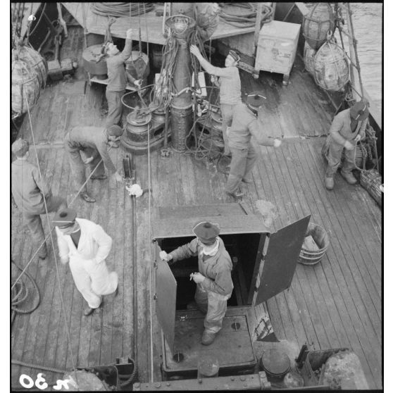 Vue en plongée sur l'équipage qui évolue sur la plage avant du chalutier de la marine marchande Roche noire, réquisitionné et armé par la Marine nationale comme dragueur de mines auxiliaire.