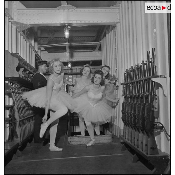 Des danseuses d'un corps de ballet traversent l'armurerie du porte-avions Béarn à bord duquel elles participent à un spectacle pour la soirée, la veille de Noël.