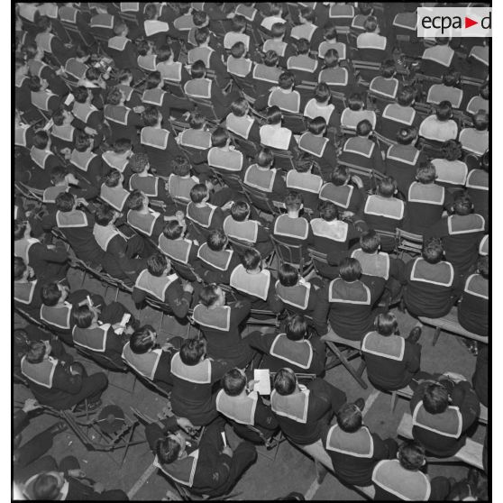 Vue en plongée sur l'équipage du porte-avions Béarn rassemblé dans une salle à l'occasion d'un spectacle donné sur le navire le soir, la veille de Noël.