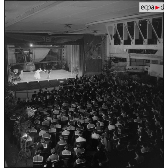 Vue en plongée sur l'équipage du porte-avions Béarn rassemblés dans une salle à l'occasion d'une représentation théâtrale donnée sur le navire le soir, la veille de Noël.