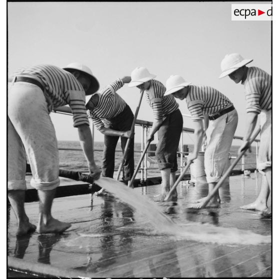 Des marins nettoient le pont du croiseur Strasbourg naviguant au large de l'Afrique occidentale française (AOF).