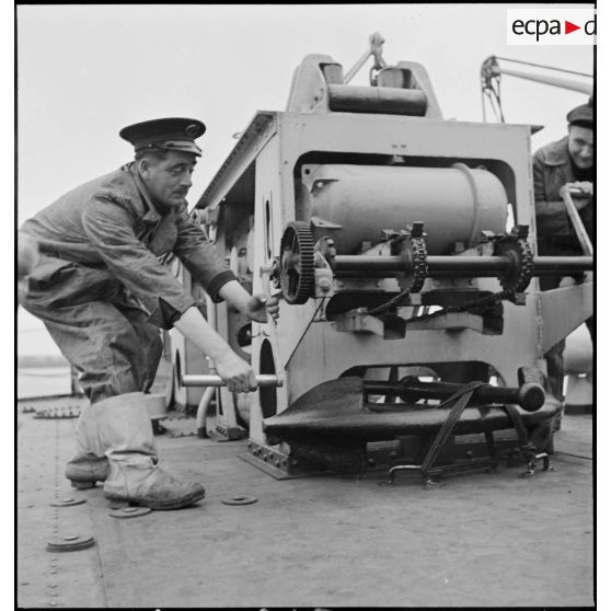 Un second maître manoeuvre le grenadeur de sillage - à chaînes à maillons avec engrenage Galle - de grenades sous-marines, à bord du torpilleur léger Branlebas.