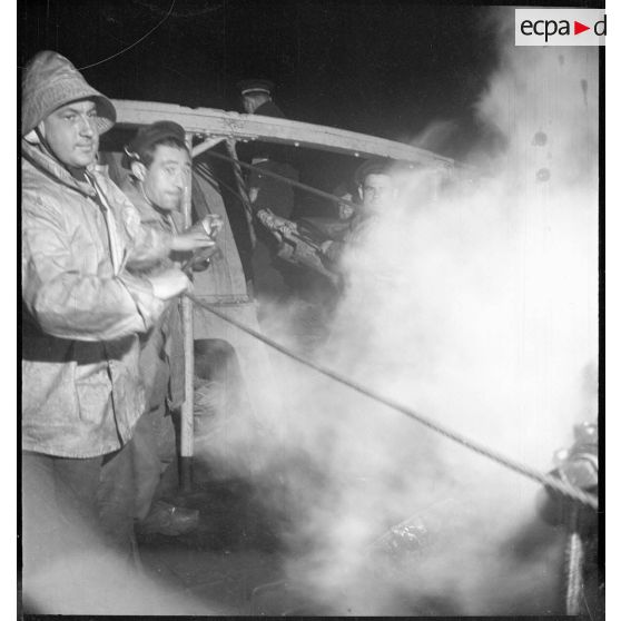 Au cours d'une mission de dragage de nuit, des marins remontent ou larguent une drague avec un treuil à vapeur à bord d'un chalutier réquisitionné par la Marine nationale pour servir de dragueur de mines.