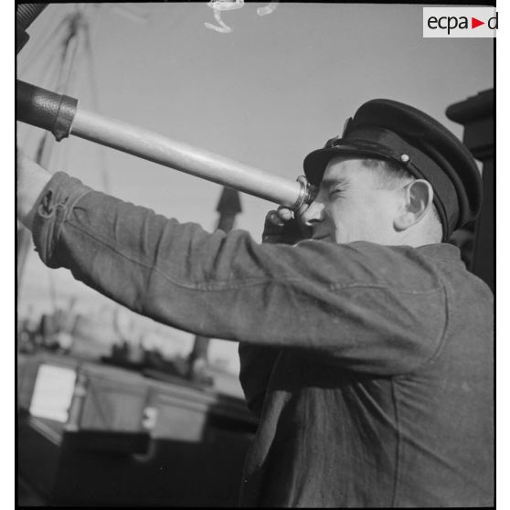 Un marin observe l'horizon à la longue vue à bord d'un chalutier réquisitionné par la Marine nationale comme dragueur de mines.