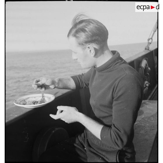 Un marin prend un repas sur le bastingage du pont d'un chalutier réquisitionné par la Marine nationale.