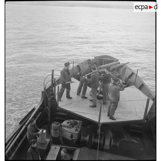 Chargement d'un canon de 75 mm sur la plage avant d'un chalutier réquisitionné et armé par la Marine nationale pour servir de dragueur de mines.