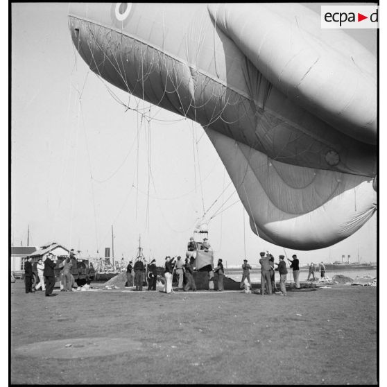 Un ballon d'observation s'élève, retenu par des marins tenant les cordages.