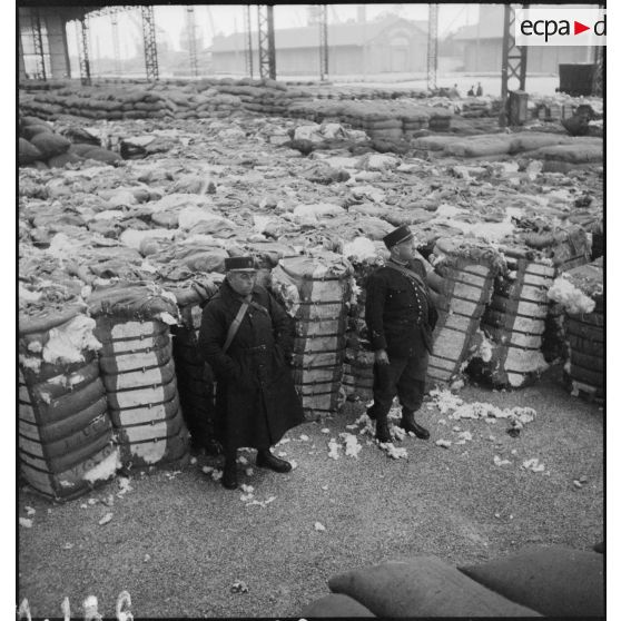 Douaniers montant la garde devant des stocks de denrées entreposées dans le port de Dunkerque, probablement saisies dans le cadre du blocus contre l'Allemagne.