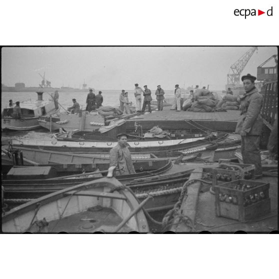 Des marins, de corvée de vivres, embarquent dans des chaloupes le ravitaillement destiné à une escadre qui mouille au large.