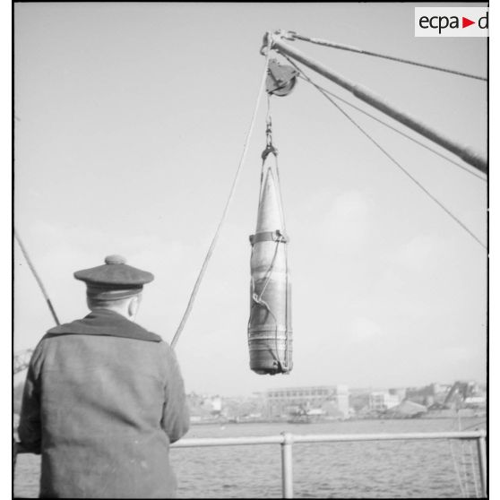 Un marin manipule un obus de 330 mm suspendu à un palan à bord du cuirassé Dunkerque.