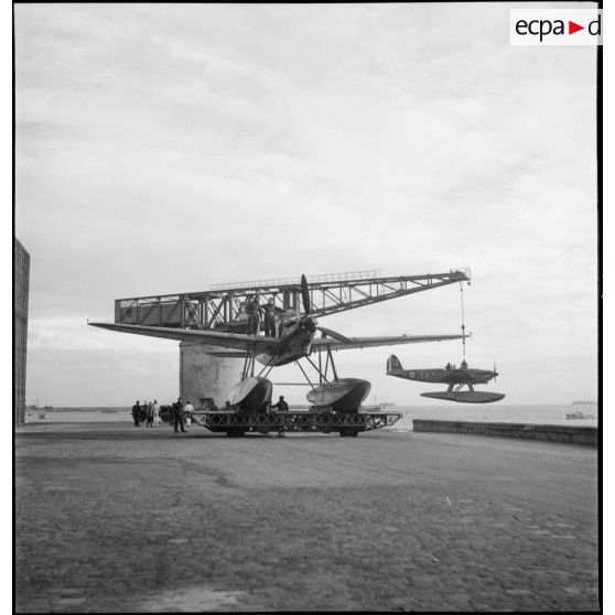 Un hydravion Latécoère 298 de l'escadrille de torpillage T3 est mis à l'eau par une grue alors qu'un autre est transporté jusqu'à un hangar de la base d'aéronautique navale de Cherbourg.