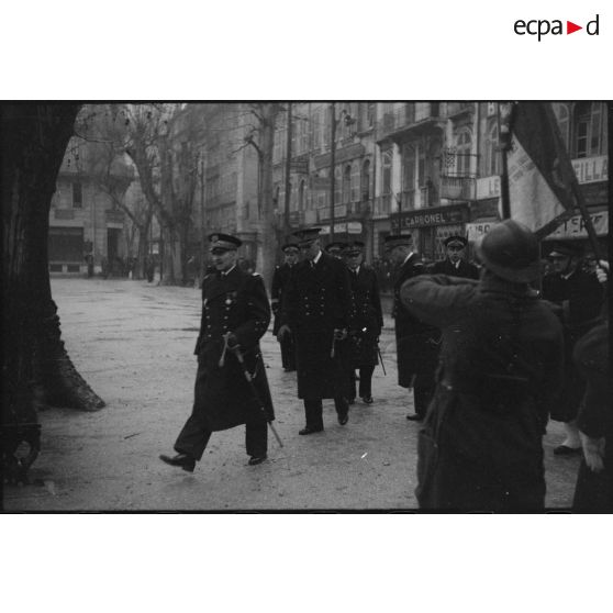 Un vice-amiral d'escadre, accompagné d'officiers de Marine, passe en revue des unités de l'armée de Terre et de la Marine lors d'une prise d'armes.