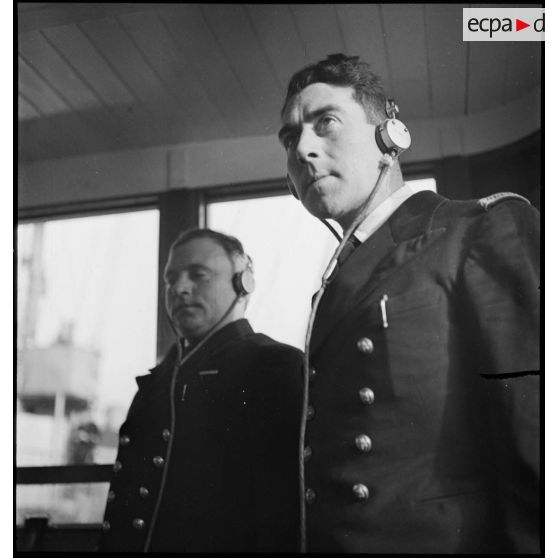 Portrait du lieutenant de vaisseau, commandant le patrouilleur La Lorientaise en compagnie d'un officier marinier, écouteurs sur les oreilles, à la passerelle de commandement.