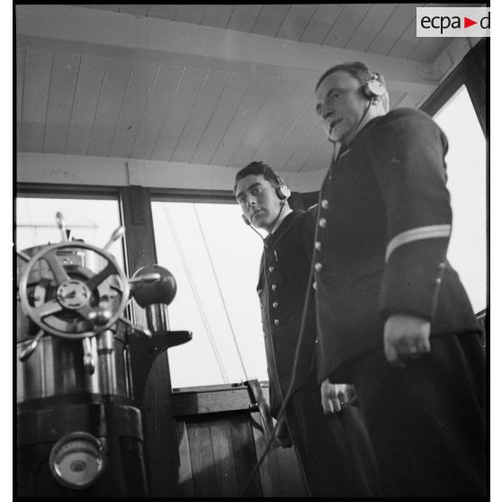 Portrait du lieutenant de vaisseau, commandant le patrouilleur La Lorientaise en compagnie d'un officier marinier, écouteurs sur les oreilles, à la passerelle de commandement.