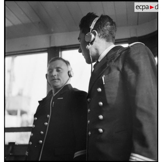 Portrait du lieutenant de vaisseau, commandant le patrouilleur La Lorientaise en compagnie d'un officier marinier, écouteurs sur les oreilles, à la passerelle de commandement.