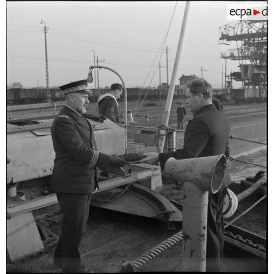 Un capitaine de corvette de la Marine nationale, qui prend possession d'un cargo danois saisi, remet le pavillon du navire à un des officiers du bord.