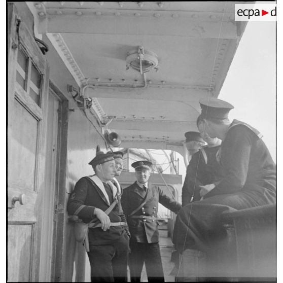 Des marins britanniques et français discutent sur le pont d'un navire marchand saisi par la Royal Navy et remis à la Marine nationale.