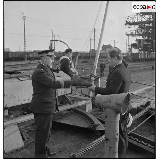 Un capitaine de corvette de la Marine nationale, qui prend possession d'un cargo danois saisi, remet le pavillon du navire à un des officiers du bord.