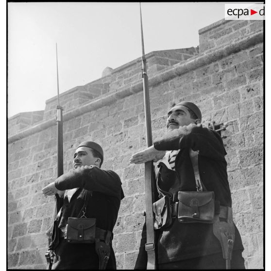 Deux sentinelles d'une unité de défense côtière, canonniers marins algériens, dits Baharia, sont en faction au fort de Mers-el-Kébir et  présentent les armes.