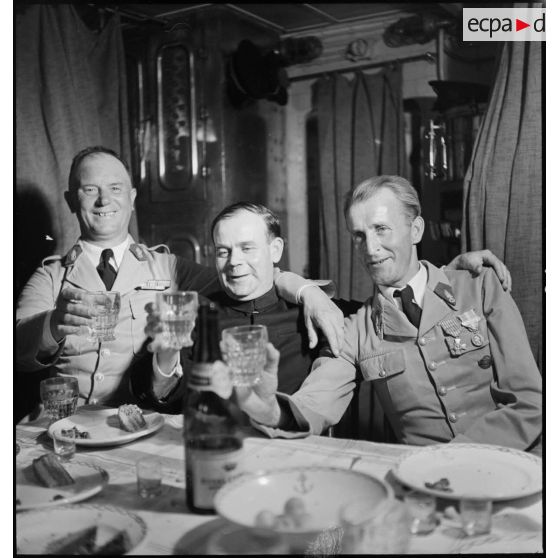 Des sous-officiers du 1er régiment étranger d'infanterie (REI) trinquent avec un aumônier lors d'un repas à bord du contre-torpilleur L'Indomptable.