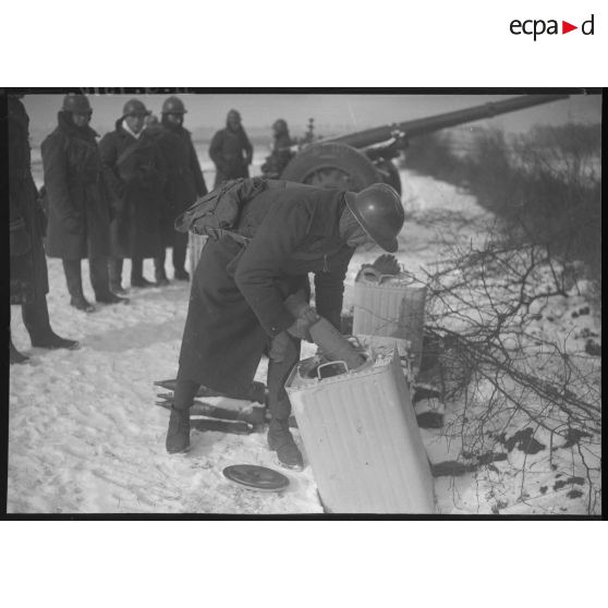 Des artilleurs se servent en appoint de charge avec en arrière-plan un canon de 105 mm long modèle 1936 Schneider.