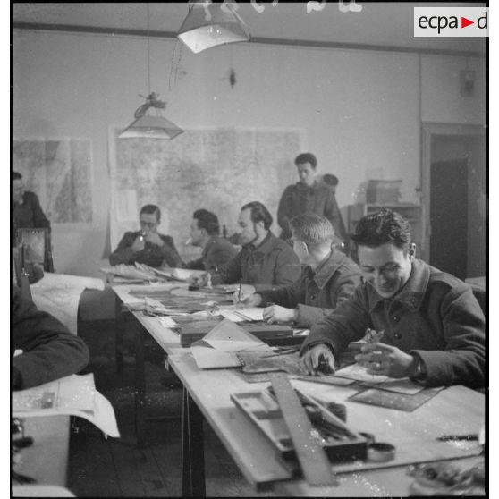 Plan général d'une salle d'état-major où divers officiers travaillent sur des photographies aériennes.