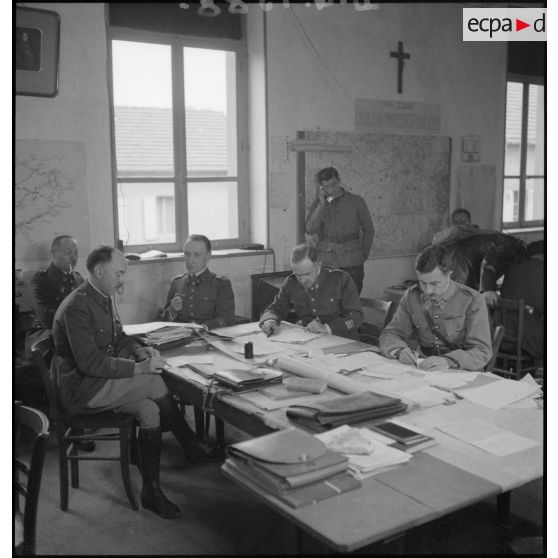 Plan général d'une salle d'état-major où divers officiers travaillent sur des photographies aériennes.