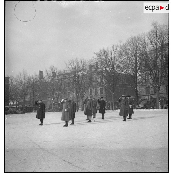 Lors d'une cérémonie militaire le général d'armée Réquin au garde-à-vous salue entouré par divers officiers.