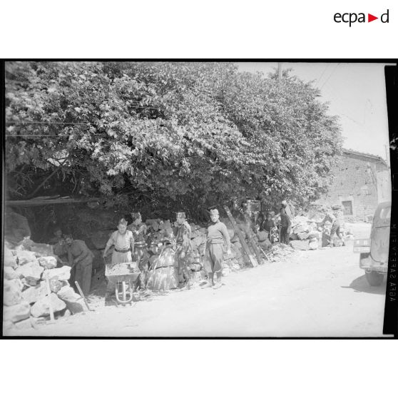 Dans un village des soldats effectuent un travail de cantonnier sur le bord d'une route à l'entrée d'un village.