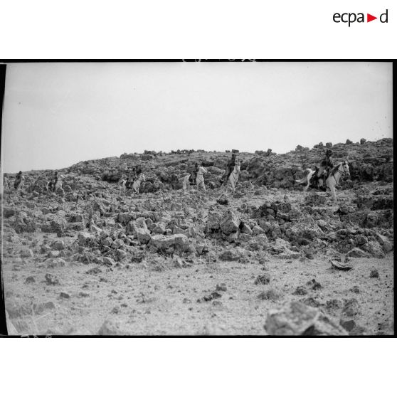 Un peloton de cavaliers druzes se déplacent au trop au milieu de rochers.