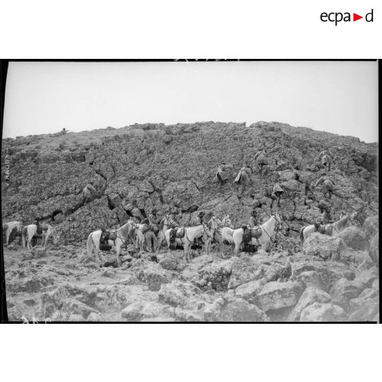 Un peloton de cavaliers druzes après avoir laissé leur monture gravissent une pente rocheuse.