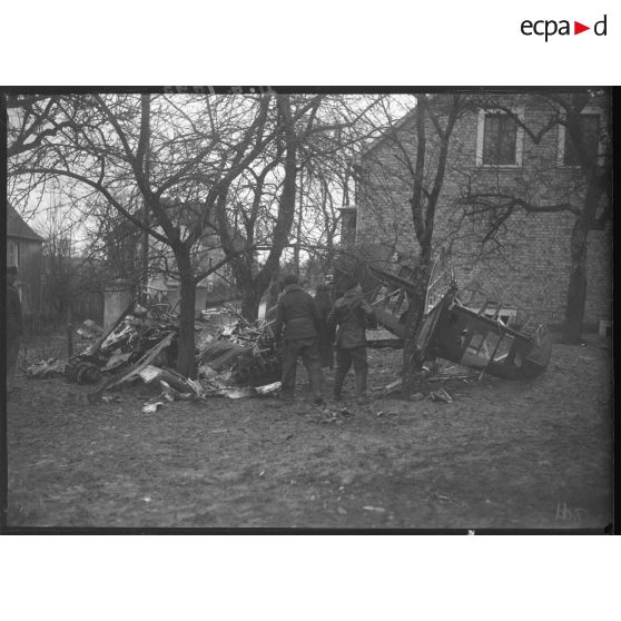 Près d'une maison, des soldats inspectent la carcasse d'un avion abattu.