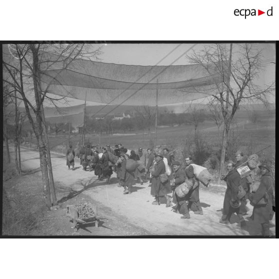 Des soldats marchent sur une route, ils sont photographiés de dos en plan général.