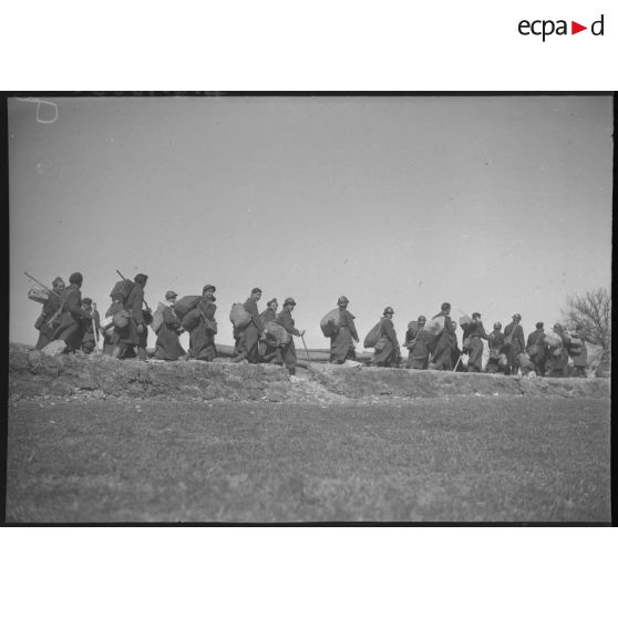 Des soldats marchent sur une route, ils sont photographiés de profil en plan général.