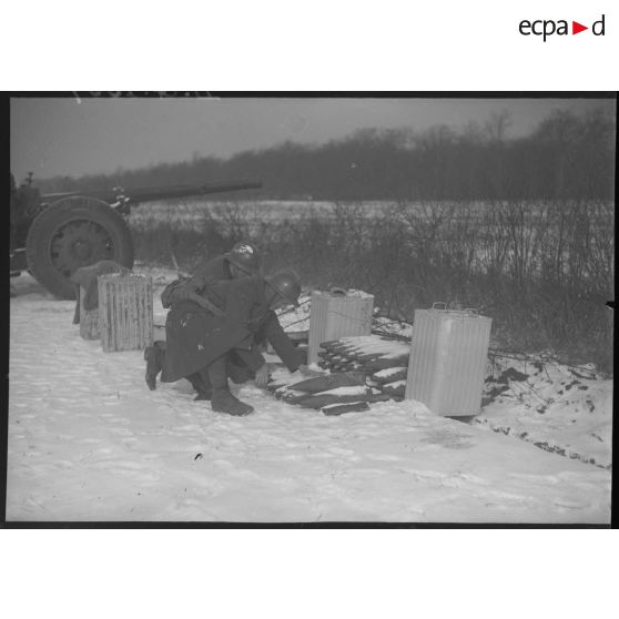 Des artilleurs se servent en obus de 105 mm avec en arrière-plan un canon de 105 mm long modèle 1936 Schneider.