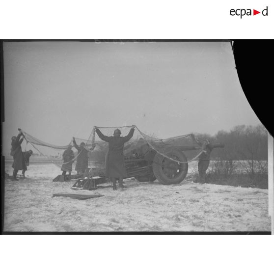 Des artilleurs mettent en place un filet de camouflage au-dessus d'un canon de 105 mm long modèle 1936 Schneider.